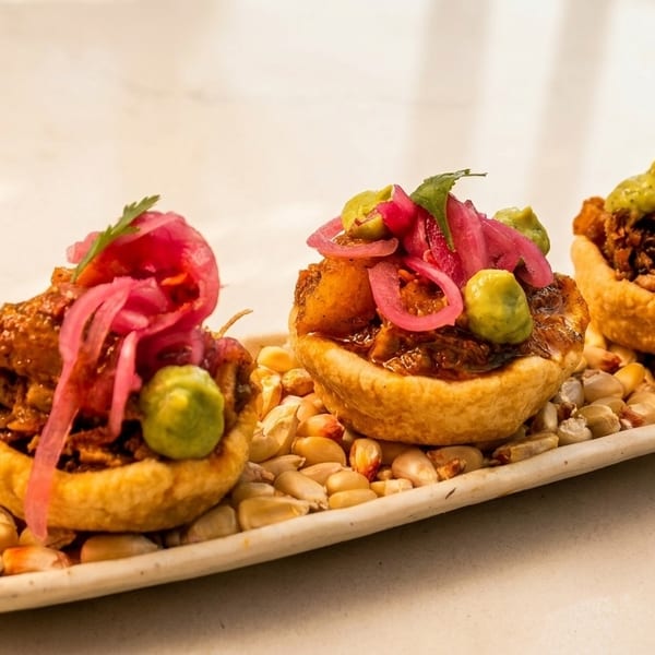 Three mini tacos with meat, pickled onions, and green sauce on a bed of corn kernels.