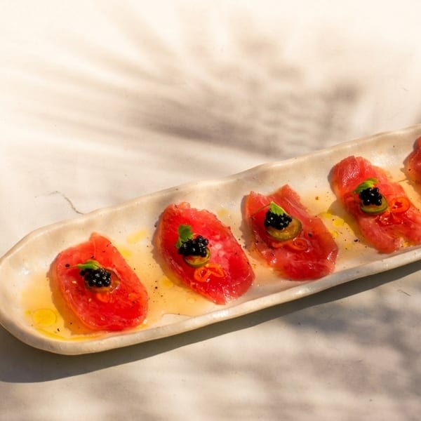 Five slices of tuna sashimi with caviar and jalapeño on a long white plate.