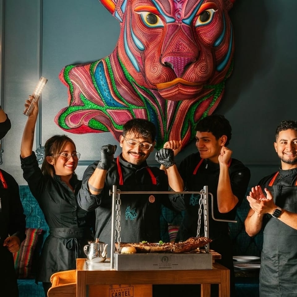 Restaurant staff celebrating around a grill with food, under a colorful jaguar art piece.