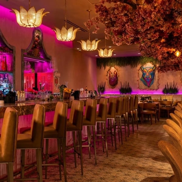 A vibrant restaurant interior with a pink-lit bar, lotus chandeliers, and a ceiling covered in red flowers.