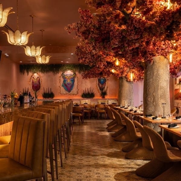 A luxurious restaurant interior with a long bar, dining tables, and a large tree with pink blossoms.