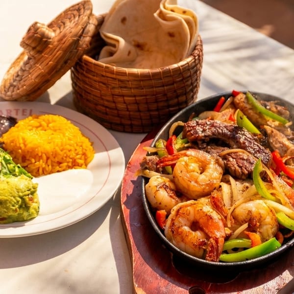 Sizzling fajitas with shrimp, steak, and vegetables, alongside rice, beans, guacamole, and tortillas.